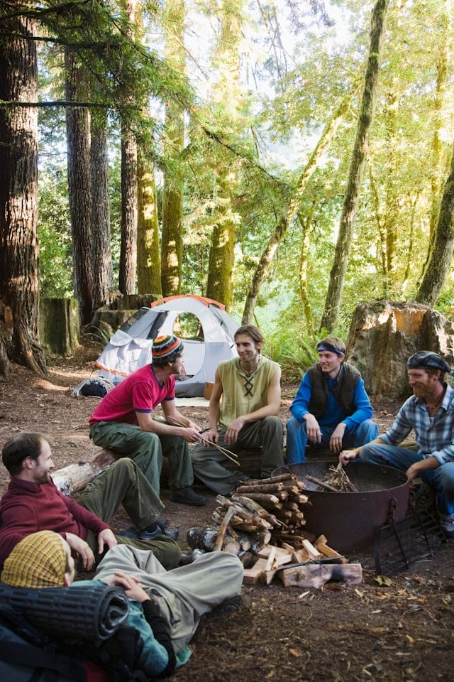 Kollegen sitzen gemeinsam am Lagerfeuer im Wald